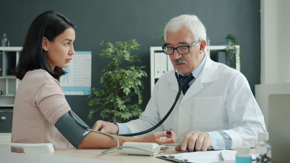 Dr. Bell takes a woman's blood pressure at his desk