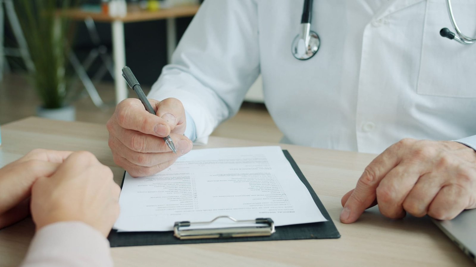 A doctor fills in a patient's chart on a clipboard across the desk
