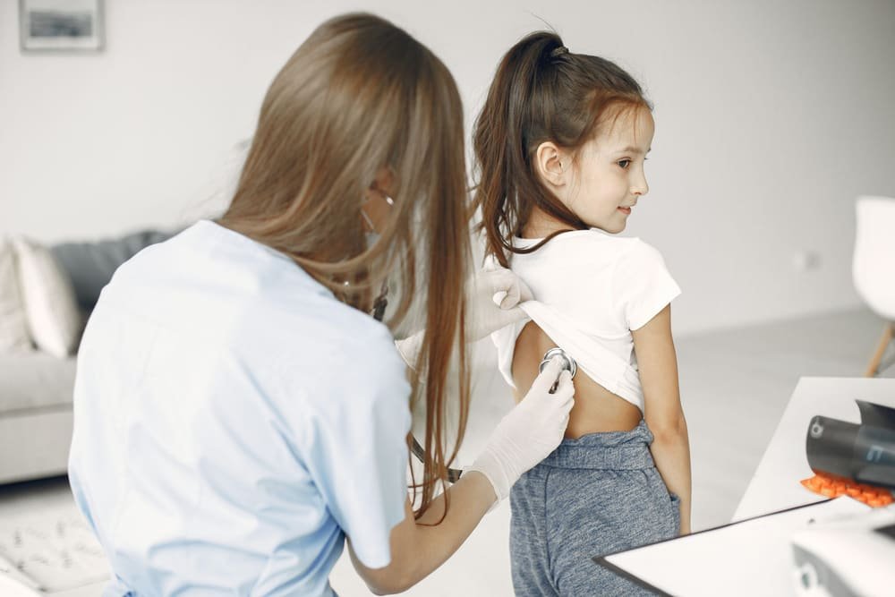 Lauren Ortiz listens to a girl's back with a stethoscope during a sick visit