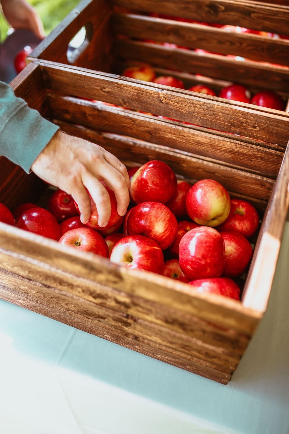 A hand lifting a red apple from a wooden crate full of apples