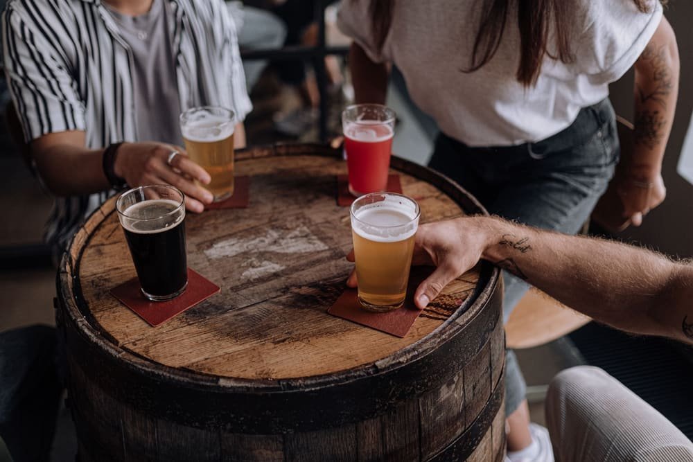 Friends setting four beers on a barrel table