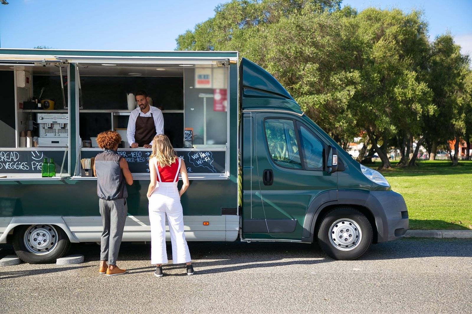 Two customers ordering at the window of a dark green food truck