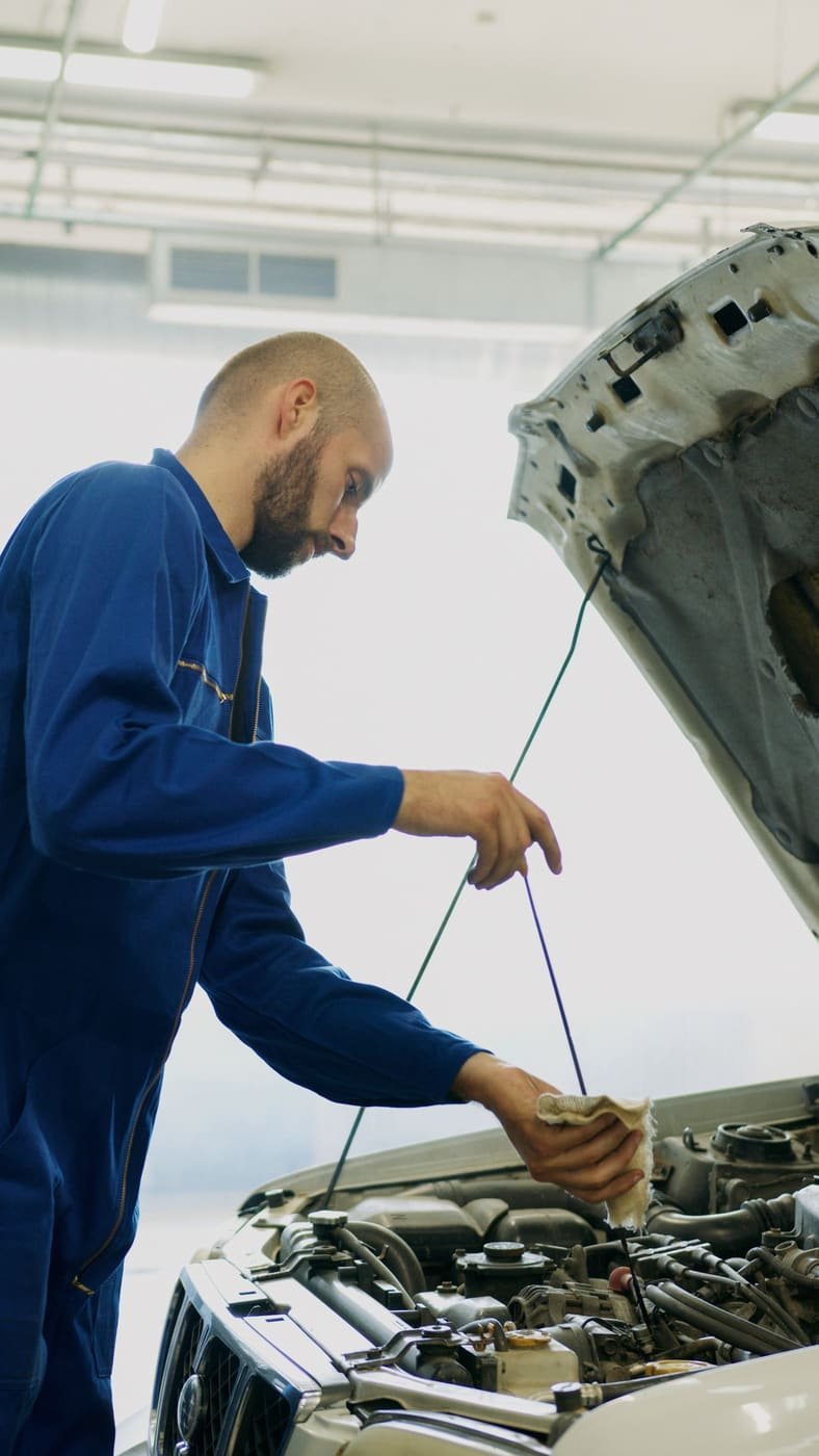 A mechanic checking the oil dipstick under an open hood