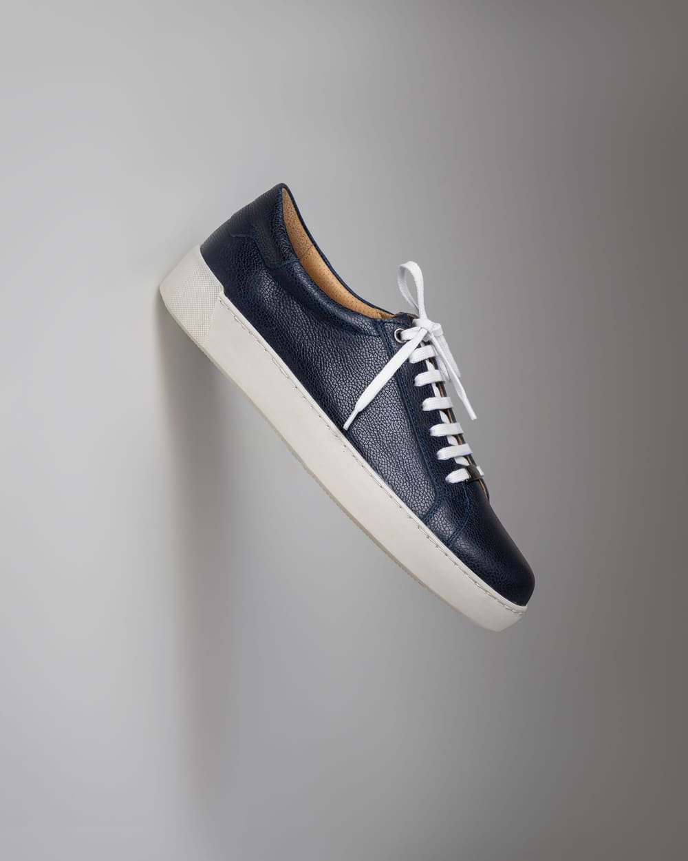 A navy leather court sneaker with a white sole against a gray wall