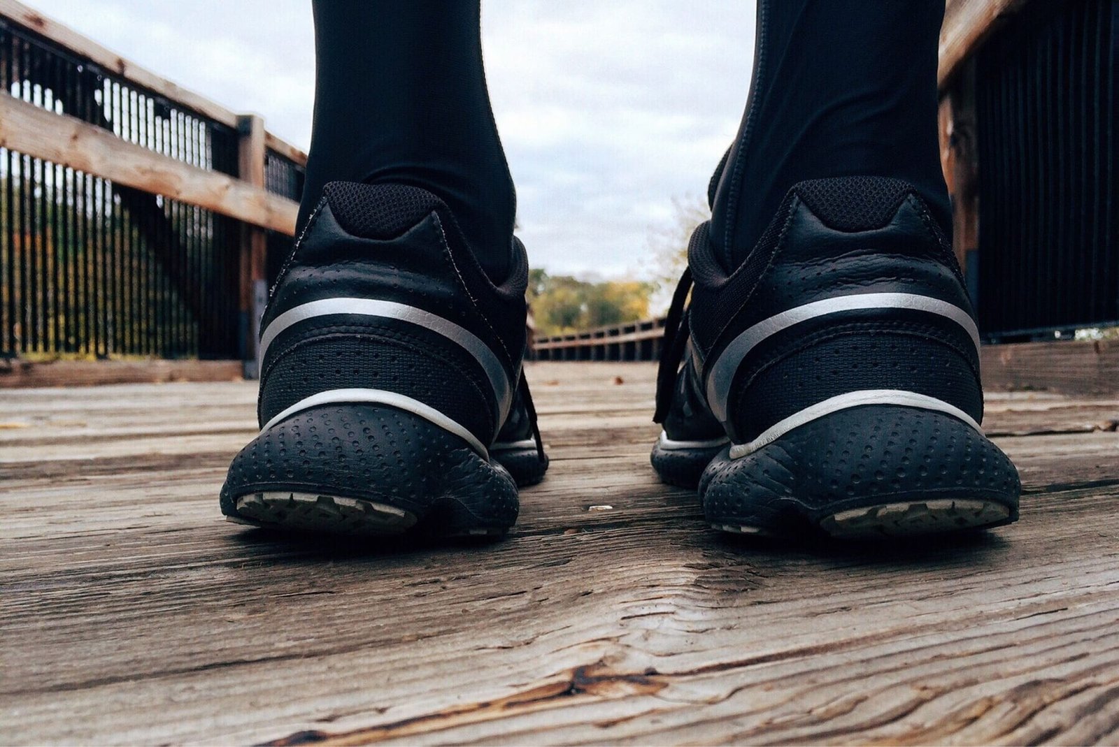 Black running shoes on a wooden footbridge, seen from behind