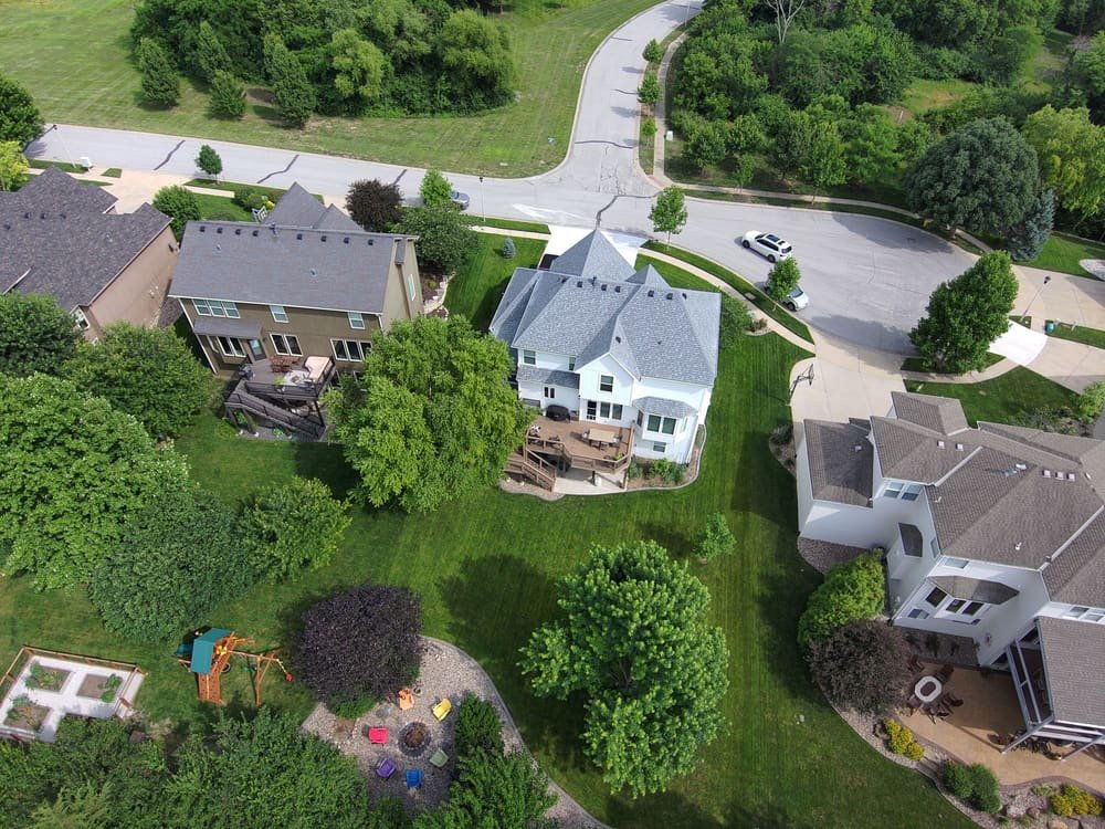 A neighborhood from the air: brick houses, curving streets and big green lawns between rows of trees