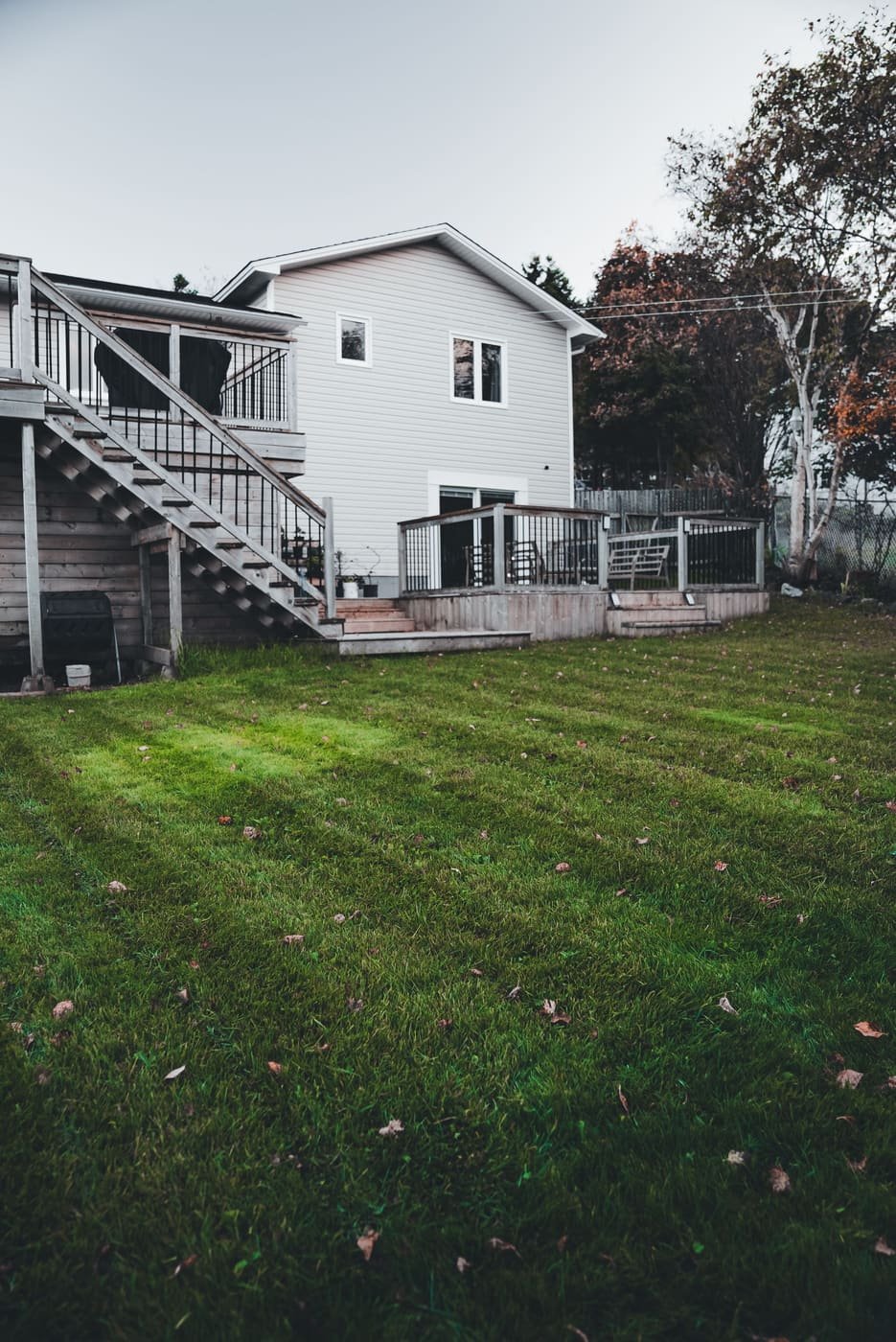 A striped backyard lawn below a wooden deck and stairs on a white house
