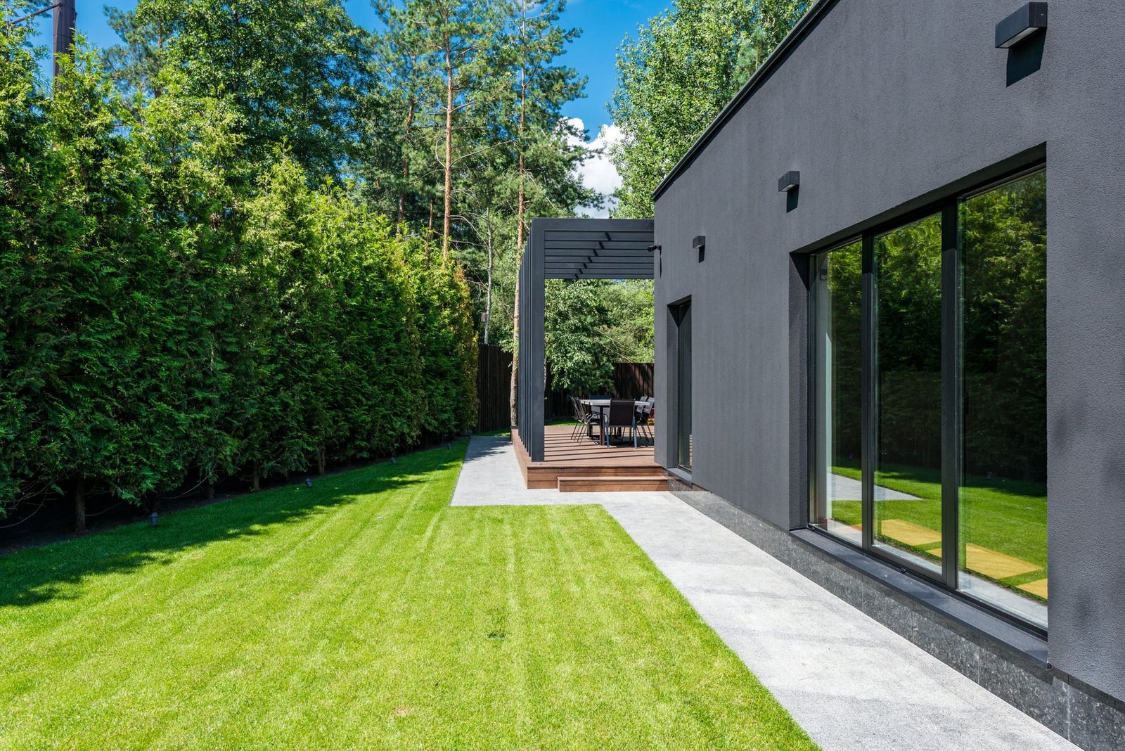 A freshly mowed lawn with light and dark stripes beside a dark modern house and a tall green hedge