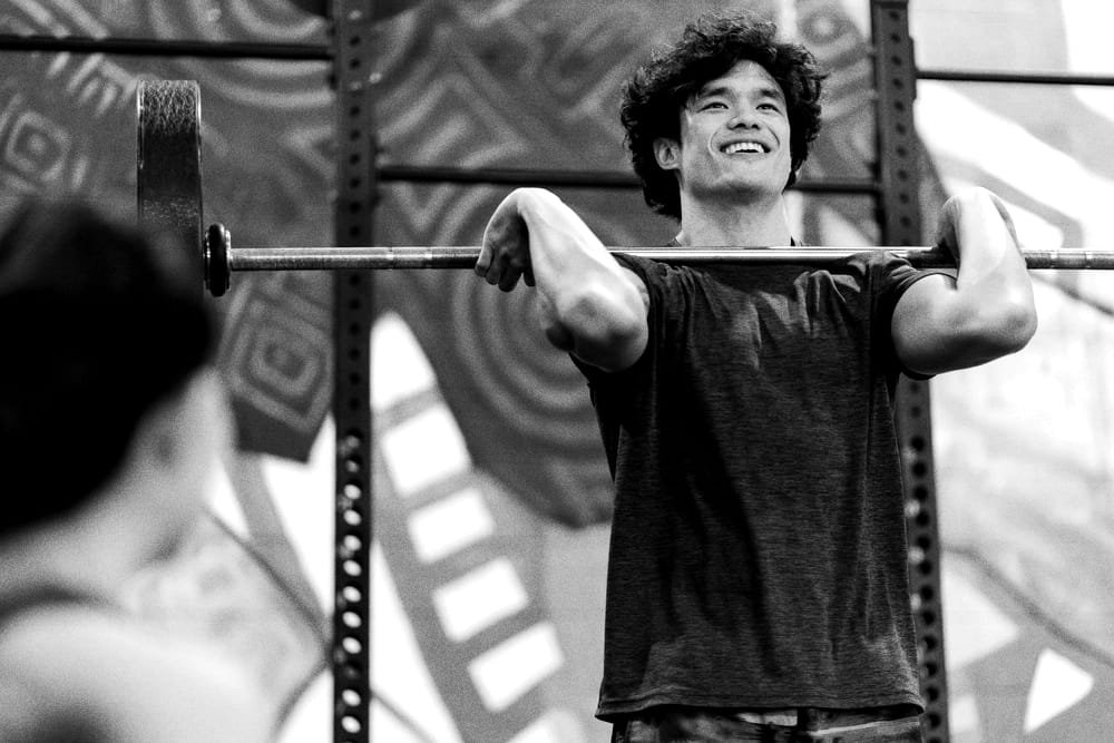 Coach Theo Park holding a barbell in the front rack, smiling