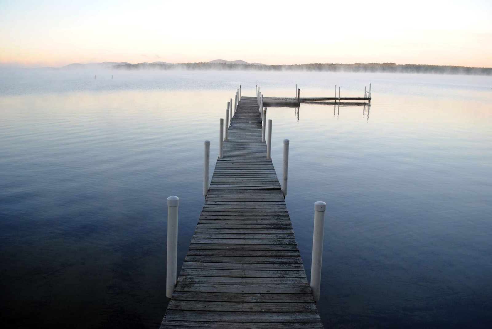A wooden pier running out into a calm lake at dawn