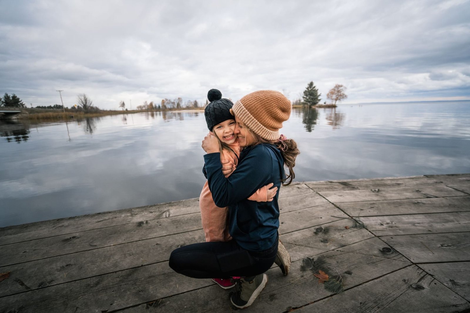 A mother hugging her laughing daughter on a dock at the lake