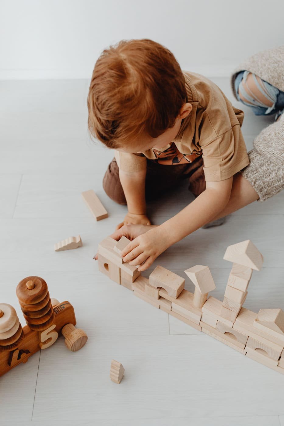 A child kneeling on a light floor, building with plain wooden blocks