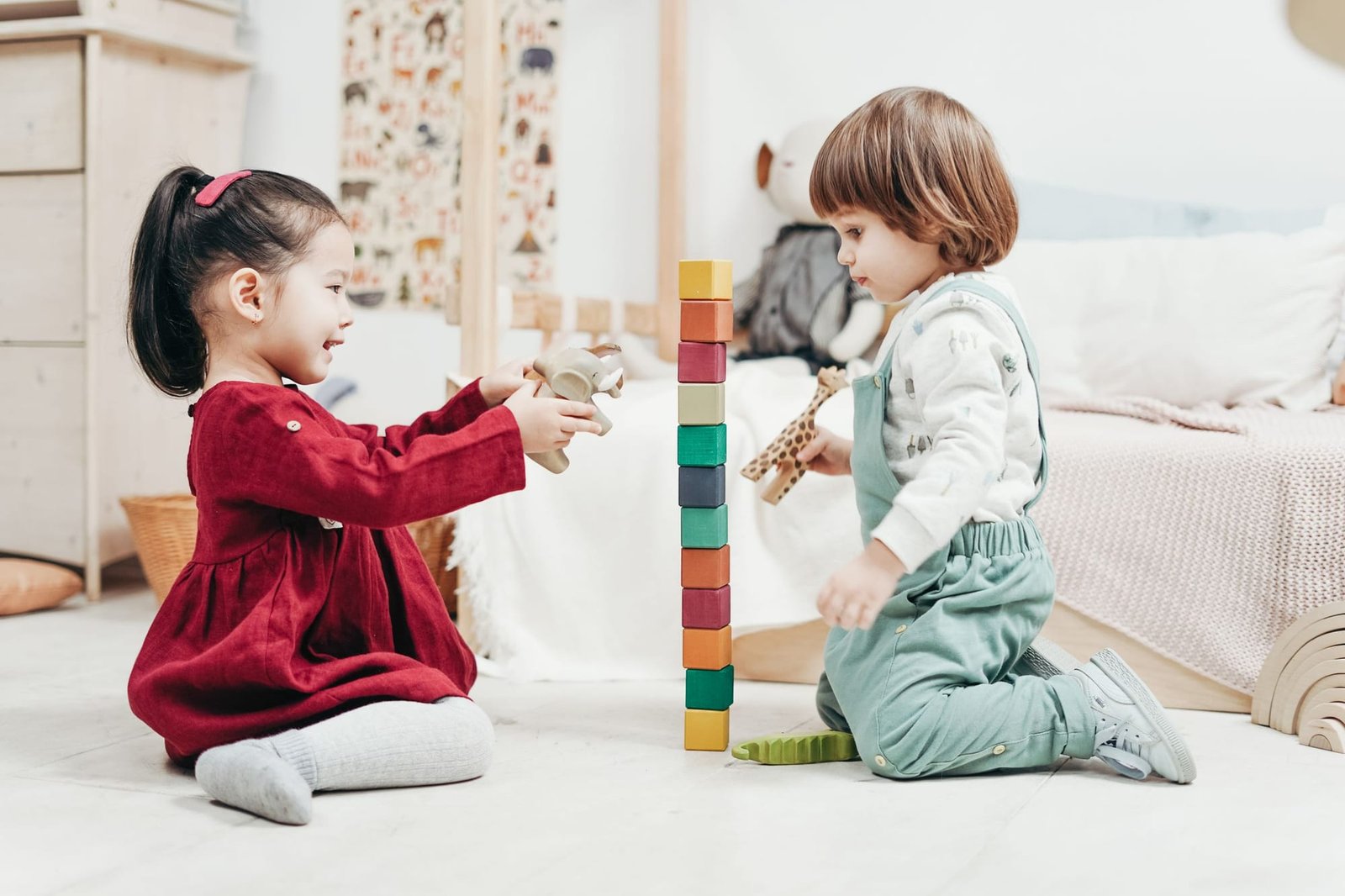 Two toddlers on the floor beside a tall tower of colored blocks