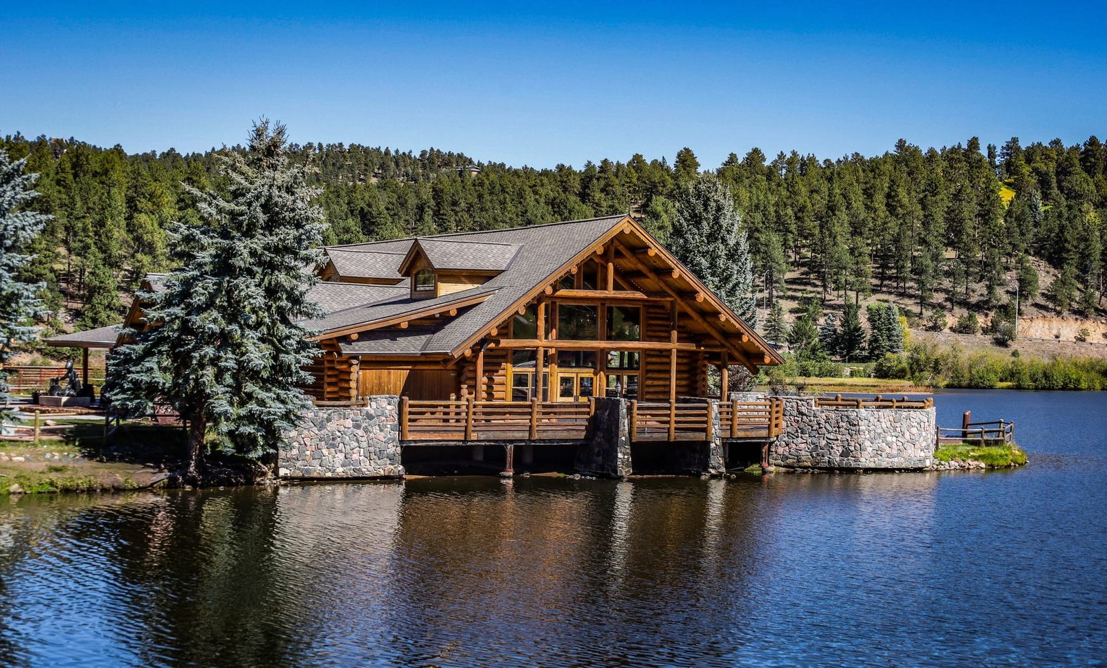 Cedar Lodge, a log lodge with a stone and timber deck over the lake, pine hills behind it