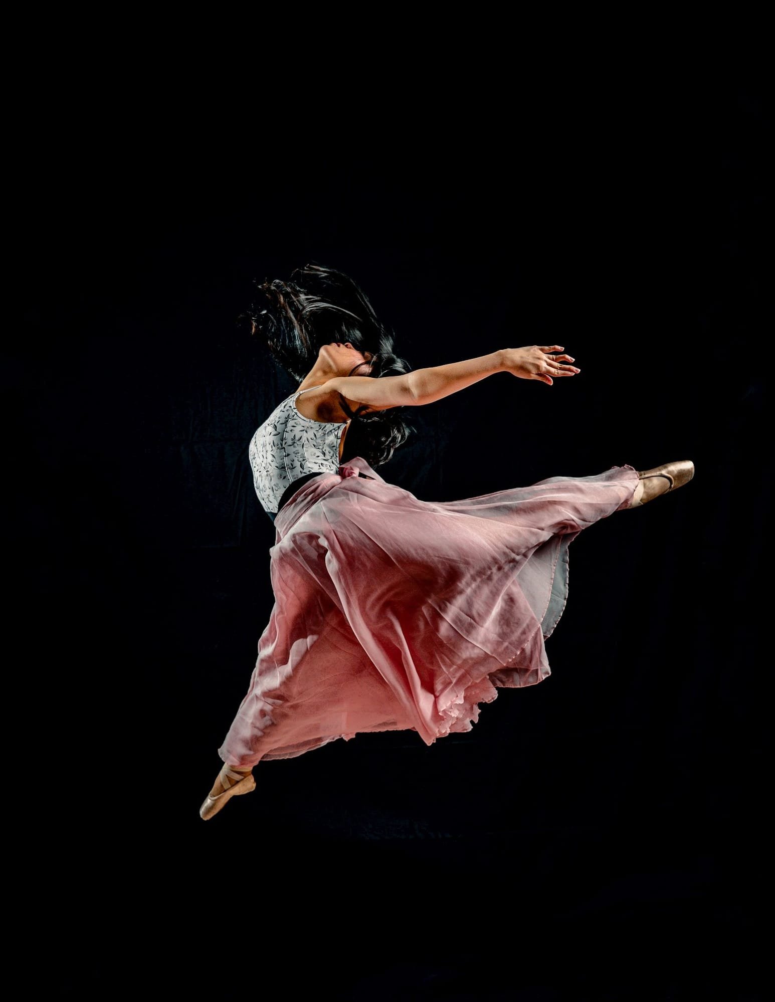 A dancer in a pink skirt in the middle of a leap