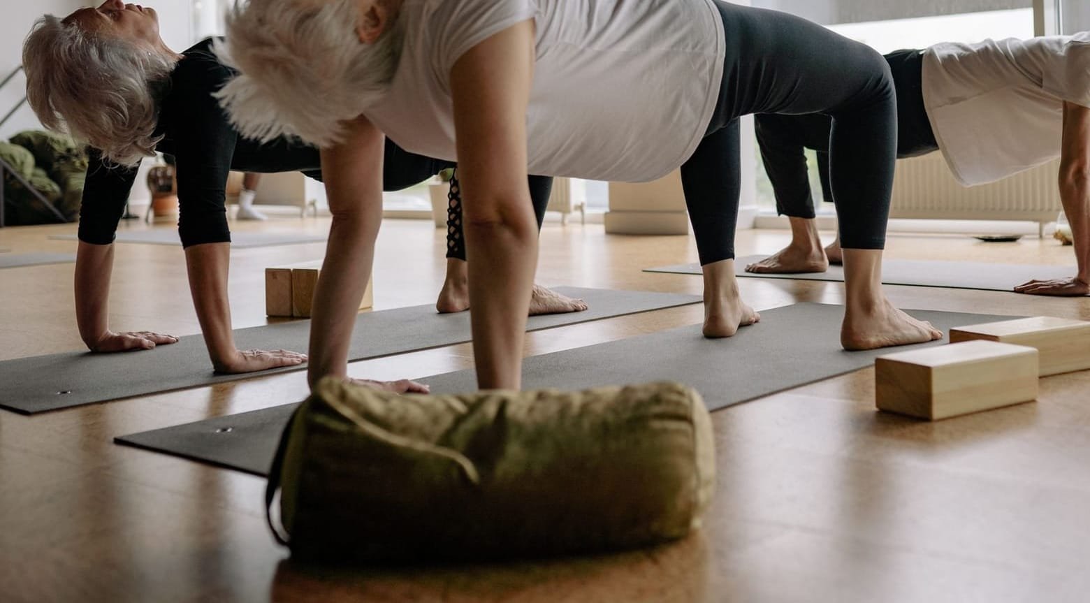 Older students holding a slow pose with blocks and a bolster