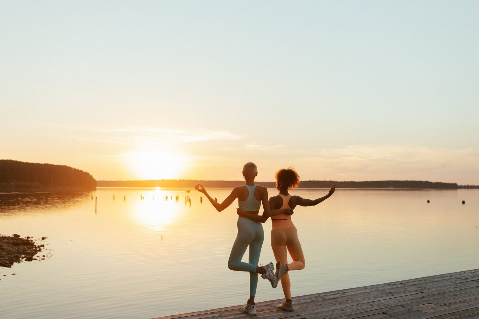 Two students in tree pose on the lakeside deck as the sun sets over the lake