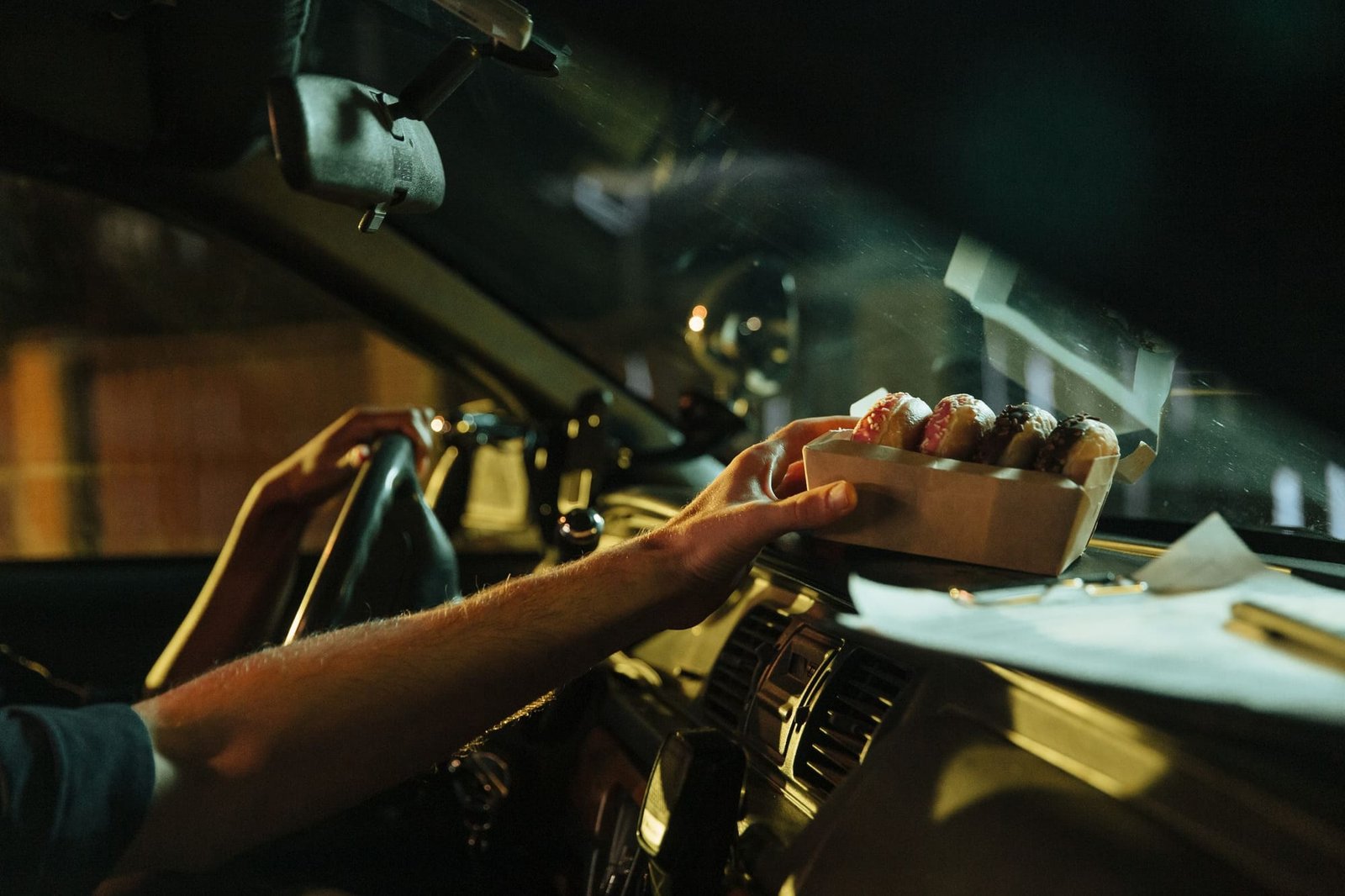 A driver sets a box of donuts on the dashboard in early light
