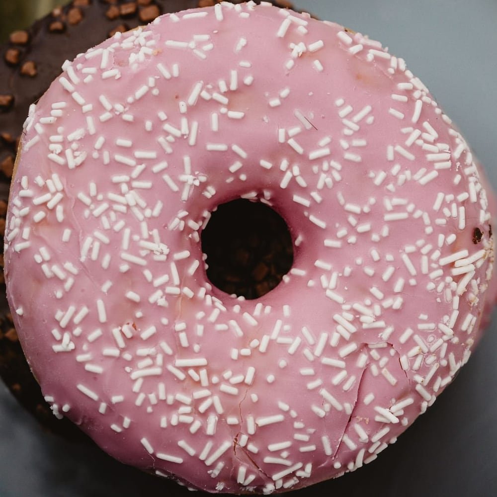 A pink iced donut covered in white sprinkles