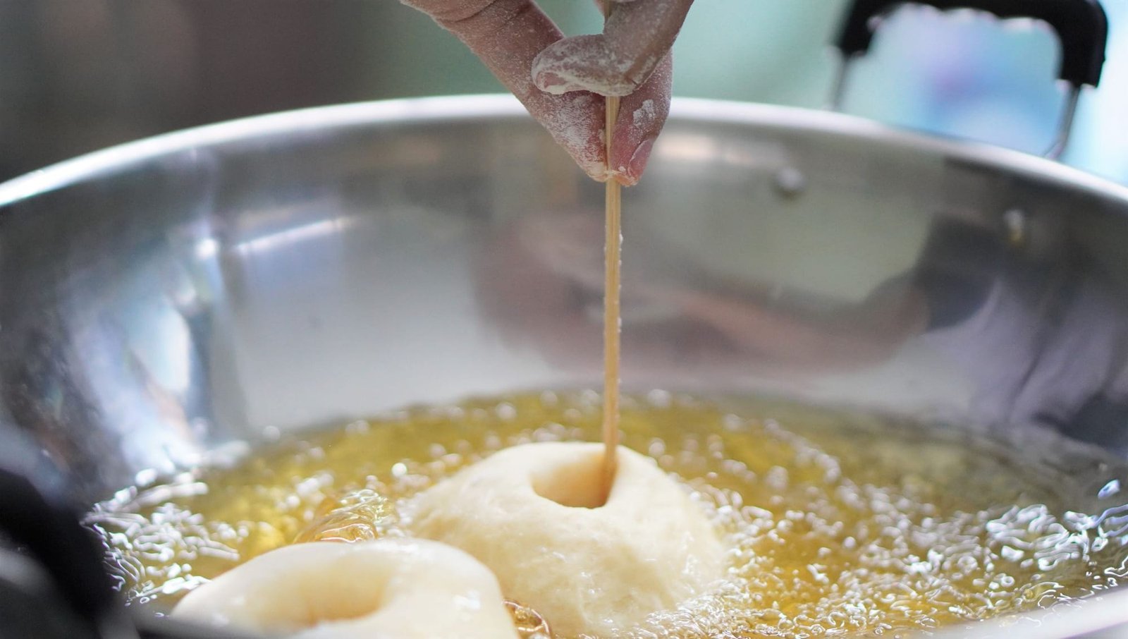 A hand turning a ring of dough in hot oil