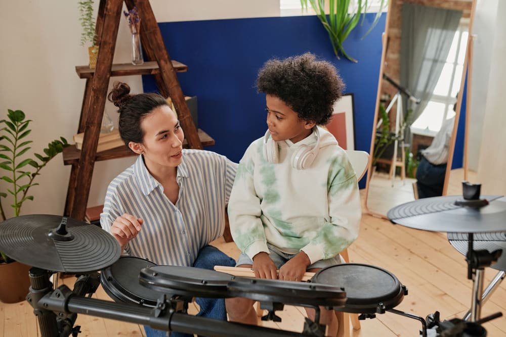 A drum teacher talking with a boy seated at an electronic drum kit