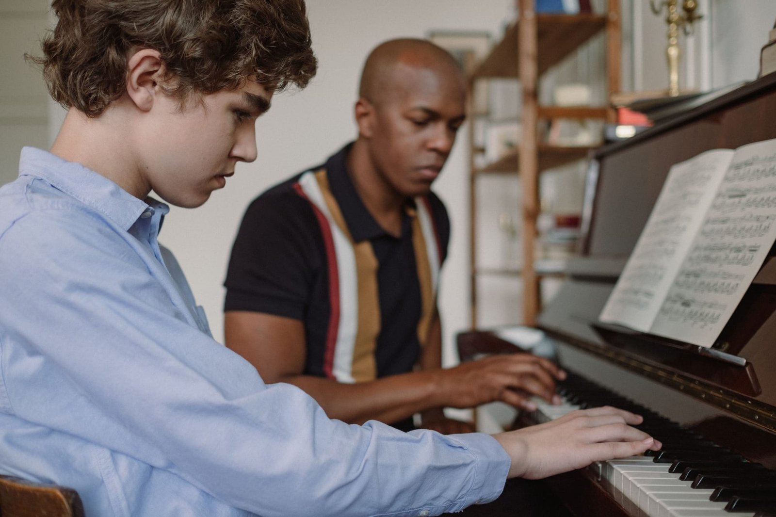 A teacher and a teenage student playing an upright piano together