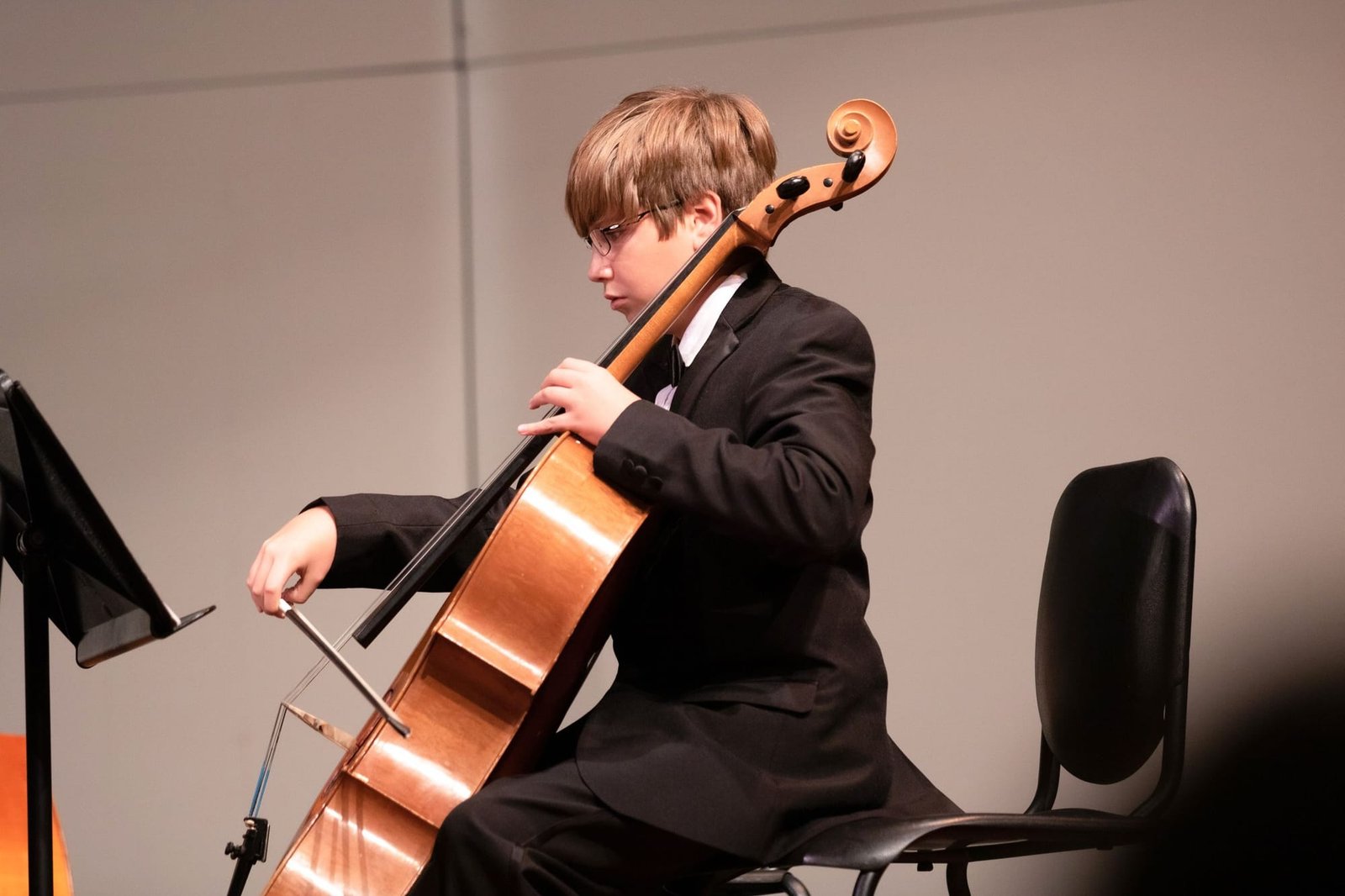 A boy in a black suit playing the cello on the recital stage