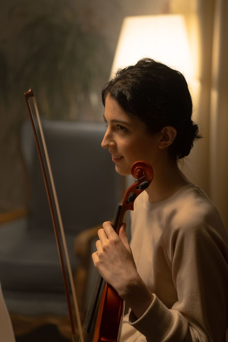 A violin teacher holding her violin and bow in warm lamp light