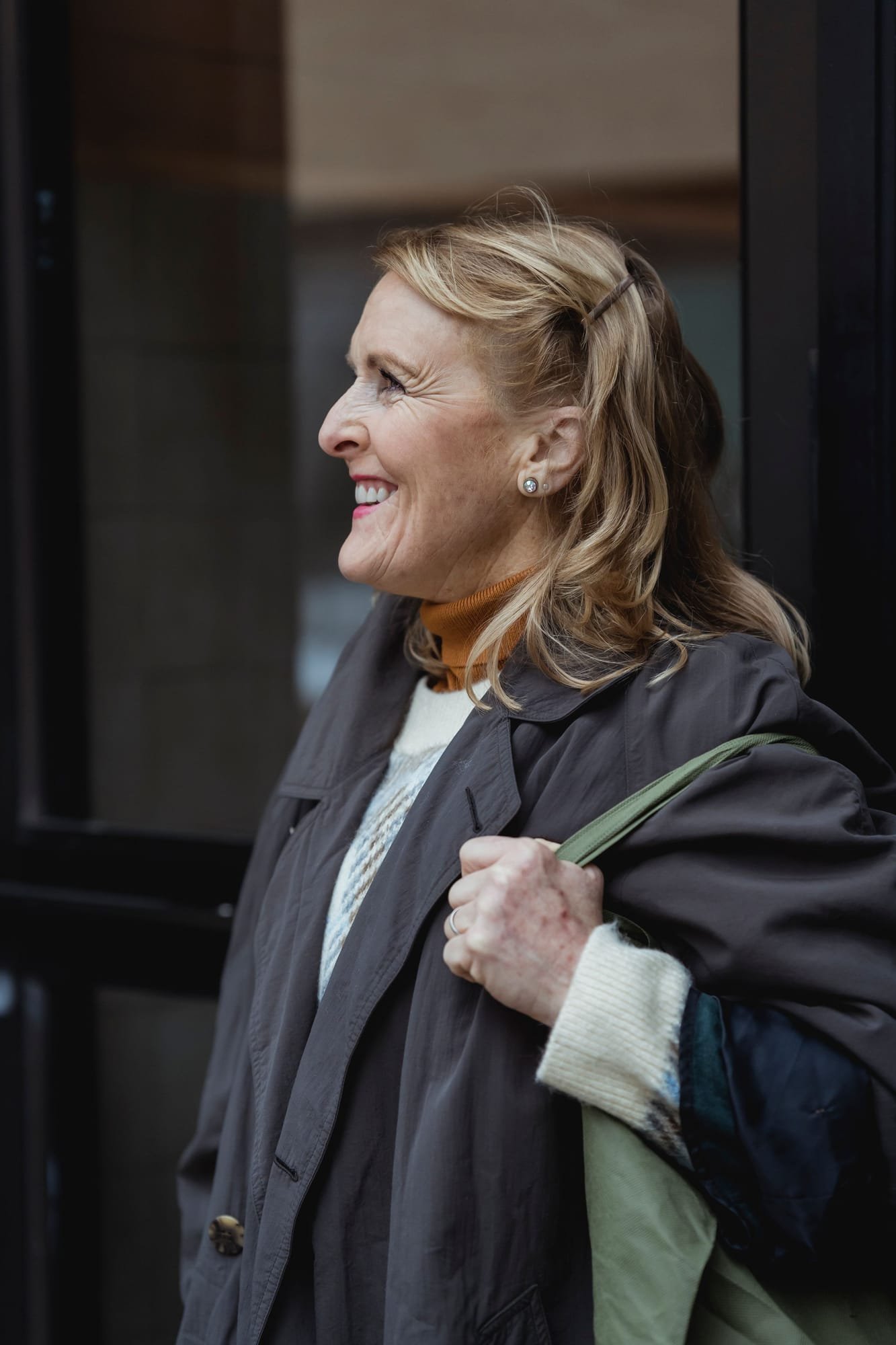 Dana Whitfield, smiling, in a dark coat with a tote bag on her shoulder