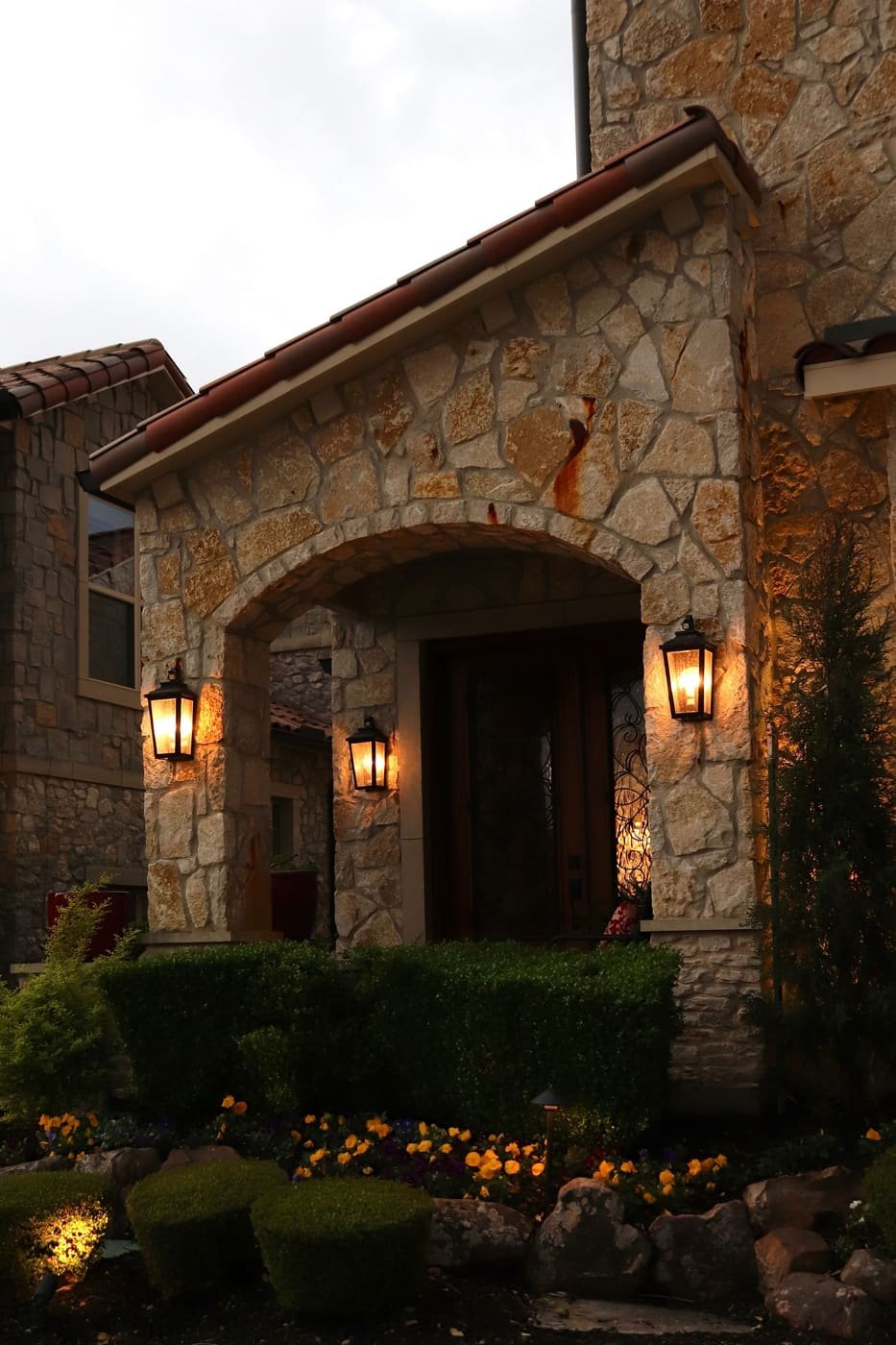 An arched stone entry with two lanterns lit at night, in Southlake