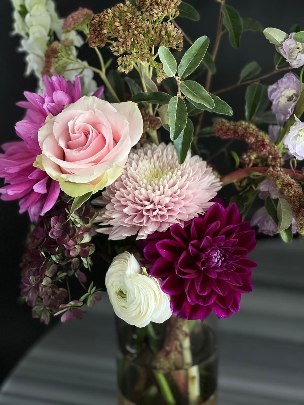A dark bouquet with a plum dahlia, a pale pink rose and white ranunculus