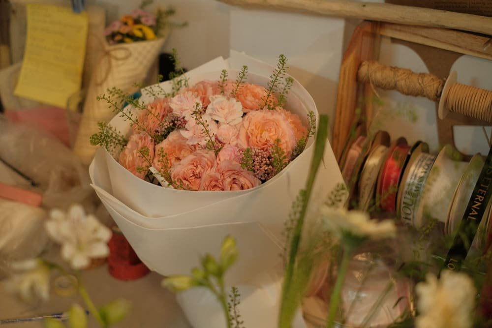 A peach bouquet wrapped in white paper on the workbench, ready to go out